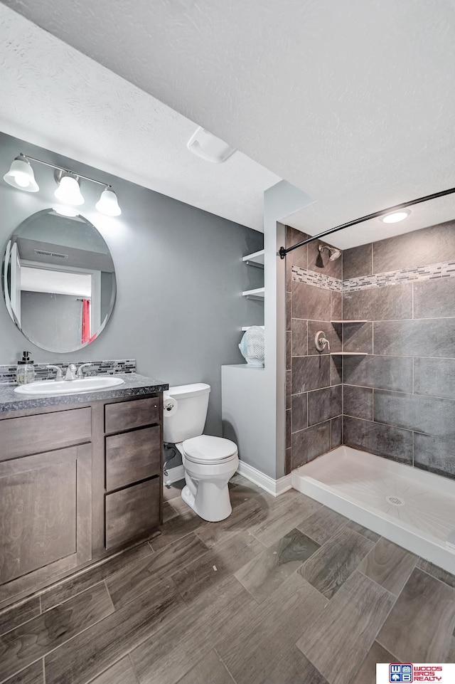 1035 Primrose Ln, Hickman, NE 68372 - bathroom featuring a tile shower, toilet, vanity, a textured ceiling, and baseboards