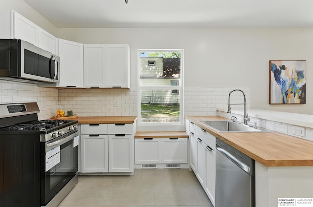3410 U St, Omaha, NE 68107 - kitchen with butcher block counters, stainless steel appliances, light tile patterned flooring, backsplash, and white cabinetry