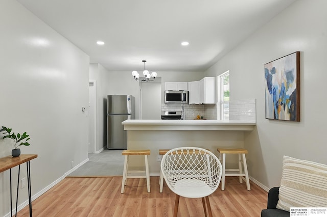 3410 U St, Omaha, NE 68107 - kitchen featuring appliances with stainless steel finishes, a peninsula, a chandelier, white cabinetry, and light wood-type flooring