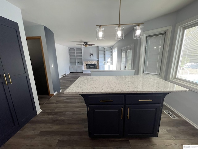13406 Erskine St, Omaha, NE 68164 - kitchen featuring a ceiling fan, dark cabinetry, a glass covered fireplace, dark wood-style flooring, and pendant lighting