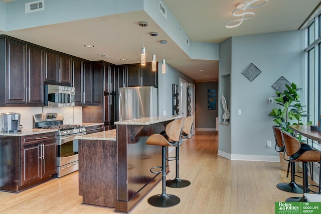 444 Riverfront Plz Unit 501, Omaha, NE 68102 - kitchen with stainless steel appliances, light wood finished floors, a kitchen breakfast bar, a center island, and light stone counters