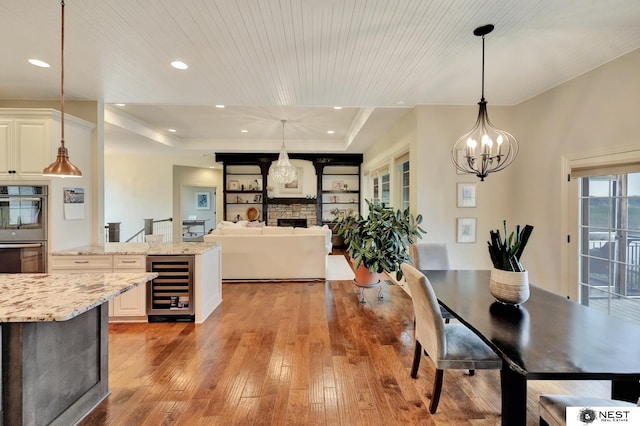 820 N 100th St, Lincoln, NE 68527 - dining area featuring beverage cooler, light wood finished floors, a chandelier, a fireplace, and a raised ceiling