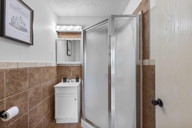 3102 Woolworth Ave, Omaha, NE 68105 - full bath featuring a stall shower, vanity, a textured ceiling, tile walls, and wainscoting