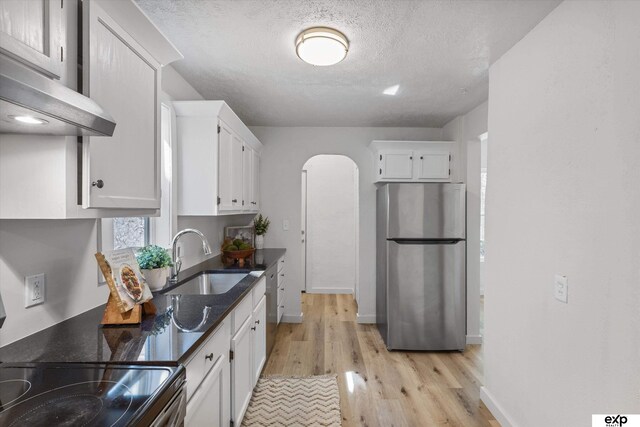 3102 Woolworth Ave, Omaha, NE 68105 - kitchen featuring freestanding refrigerator, arched walkways, range hood, white cabinets, and a textured ceiling