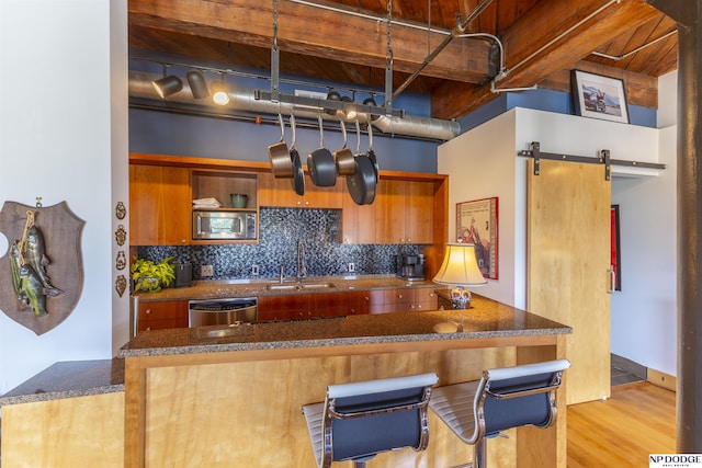 105 S 9th St Unit 308, Omaha, NE 68102 - kitchen featuring appliances with stainless steel finishes, tasteful backsplash, brown cabinetry, a barn door, and light wood-type flooring