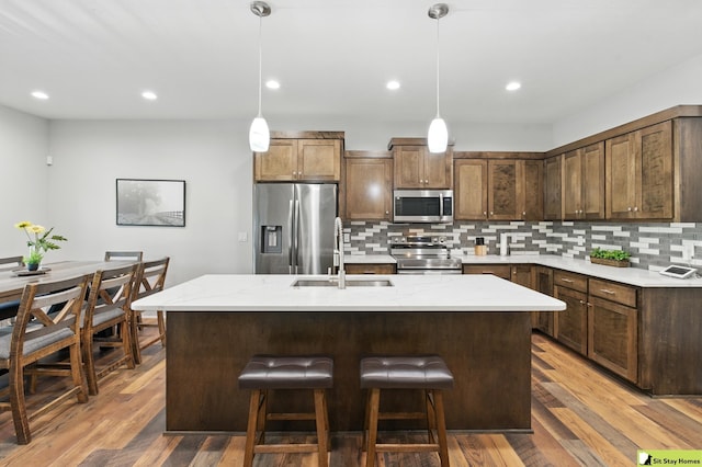 15436 Fowler Ave, Omaha, NE 68116 - kitchen with stainless steel appliances, backsplash, a center island with sink, wood finished floors, and recessed lighting