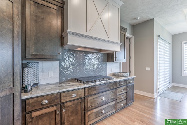 20761 Shirley St, Omaha, NE 68022 - kitchen featuring light wood-style floors, dark brown cabinetry, tasteful backsplash, stainless steel gas stovetop, and light stone countertops