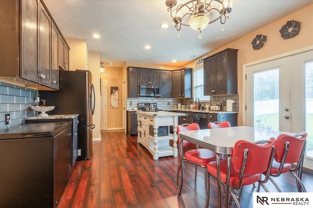16228 Virginia St, Omaha, NE 68136 - kitchen with stainless steel appliances, dark brown cabinetry, a chandelier, backsplash, and dark wood-style floors