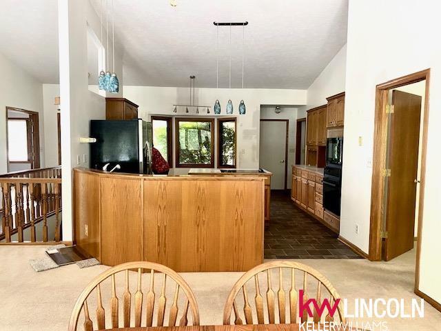2930 Drawbridge Ct, Lincoln, NE 68516 - kitchen with freestanding refrigerator, black oven, a peninsula, vaulted ceiling, and dark carpet