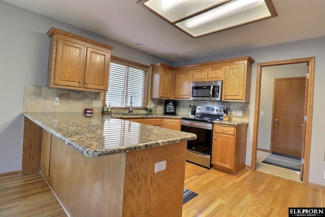 19523 Binney Cir, Elkhorn, NE 68022 - kitchen featuring appliances with stainless steel finishes, light wood-type flooring, a peninsula, and decorative backsplash