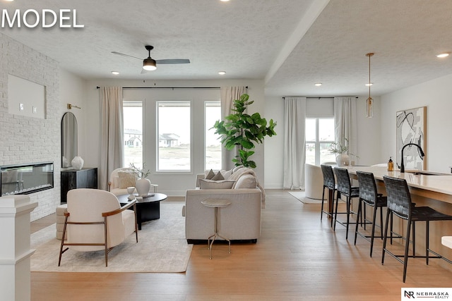 12386 Fenwick St, Papillion, NE 68046 - living room featuring a textured ceiling, light wood-type flooring, a ceiling fan, recessed lighting, and a brick fireplace