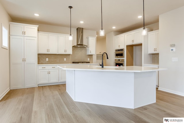 12382 Fenwick St, Papillion, NE 68046 - kitchen with wall chimney exhaust hood, light wood-style flooring, decorative backsplash, a center island with sink, and white cabinets