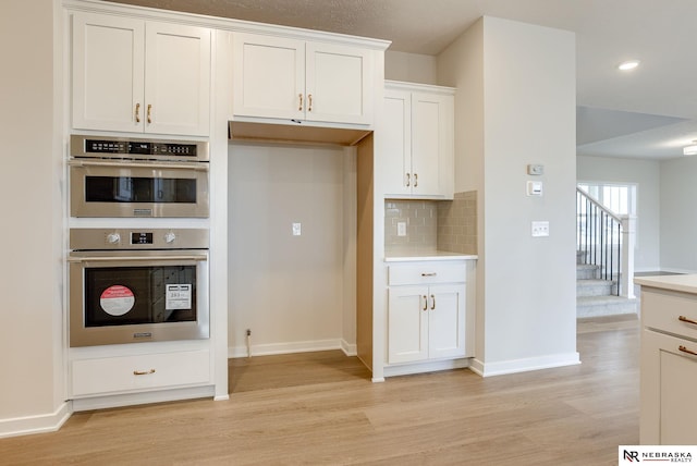 12382 Fenwick St, Papillion, NE 68046 - kitchen with light wood-style flooring, white cabinets, backsplash, light countertops, and double oven