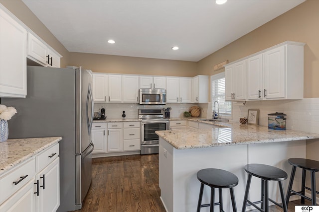 16454 Drexel St, Omaha, NE 68135 - kitchen featuring appliances with stainless steel finishes, a peninsula, white cabinetry, decorative backsplash, and dark wood finished floors