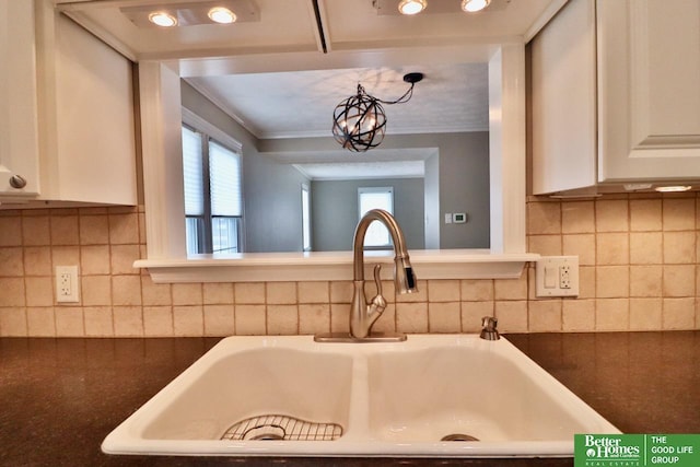 1115 S 63rd St, Omaha, NE 68106 - kitchen view of dark countertops, white cabinetry, crown molding, decorative backsplash, and a chandelier