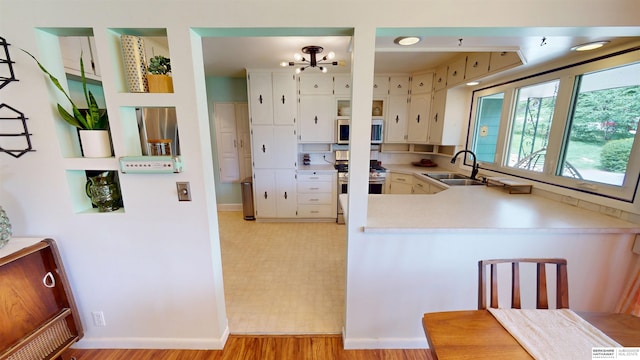 7923 Harney St, Omaha, NE 68114 - kitchen with gas range, light countertops, a peninsula, light wood-style flooring, and white cabinetry