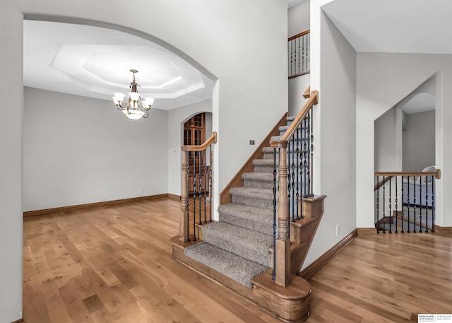 10149 Edward St, La Vista, NE 68128 - staircase featuring arched walkways, wood finished floors, a chandelier, and a tray ceiling