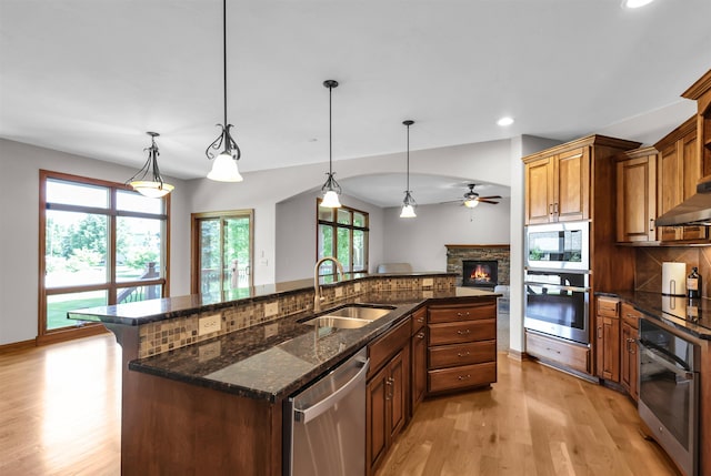 10149 Edward St, La Vista, NE 68128 - kitchen featuring appliances with stainless steel finishes, a center island with sink, light wood-style flooring, a fireplace, and decorative backsplash