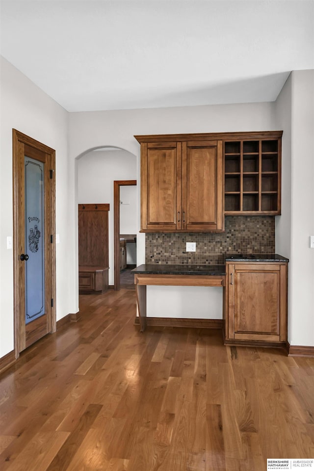 10149 Edward St, La Vista, NE 68128 - kitchen featuring dark countertops, arched walkways, brown cabinetry, open shelves, and tasteful backsplash