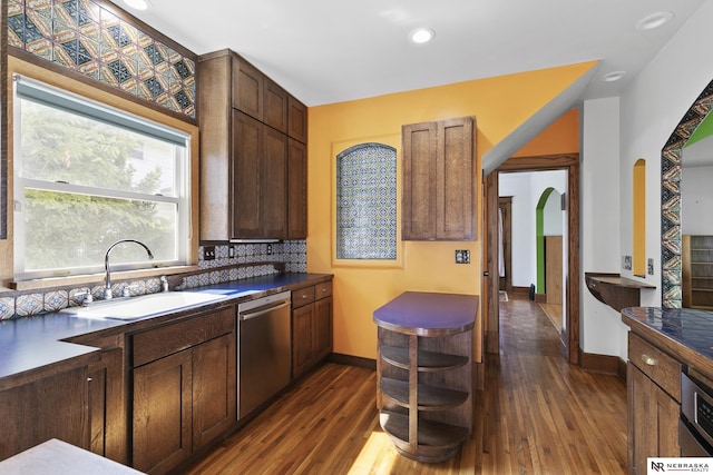 2615 C St, Lincoln, NE 68502 - kitchen featuring stainless steel dishwasher, arched walkways, dark wood-type flooring, backsplash, and dark countertops