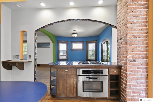 2615 C St, Lincoln, NE 68502 - kitchen featuring appliances with stainless steel finishes, tile counters, wood finished floors, arched walkways, and recessed lighting