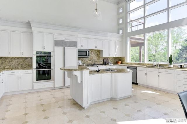 14341 Hamilton St, Omaha, NE 68154 - kitchen with stainless steel appliances, white cabinets, light stone countertops, decorative backsplash, and a towering ceiling