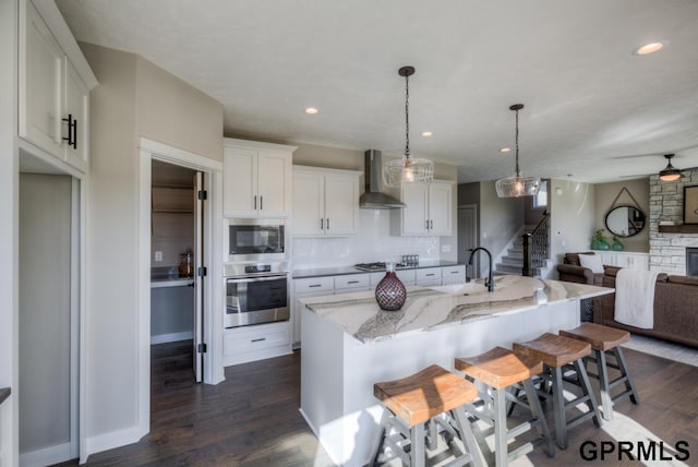 3103 N 184th St, Elkhorn, NE 68022 - kitchen featuring wall chimney range hood, stainless steel appliances, open floor plan, dark wood-style floors, and a stone fireplace
