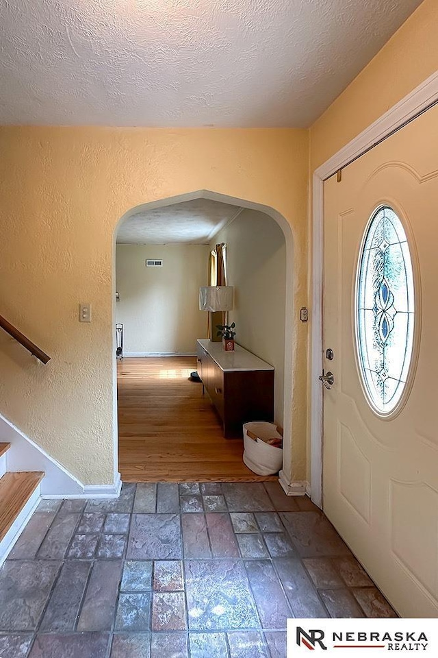 3340 N 48th Ave, Omaha, NE 68104 - foyer featuring arched walkways, stone finish flooring, a textured ceiling, stairs, and a textured wall
