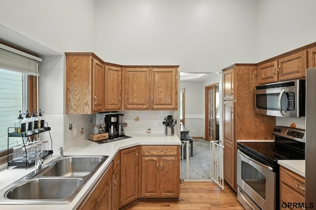 2303 N 150th Ave, Omaha, NE 68116 - kitchen with appliances with stainless steel finishes, light wood-style floors, a towering ceiling, decorative backsplash, and brown cabinets