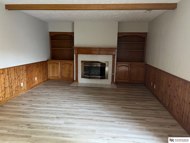 6211 S 150th St, Omaha, NE 68137 - unfurnished living room featuring wooden walls, wainscoting, light wood-type flooring, a tile fireplace, and a textured ceiling