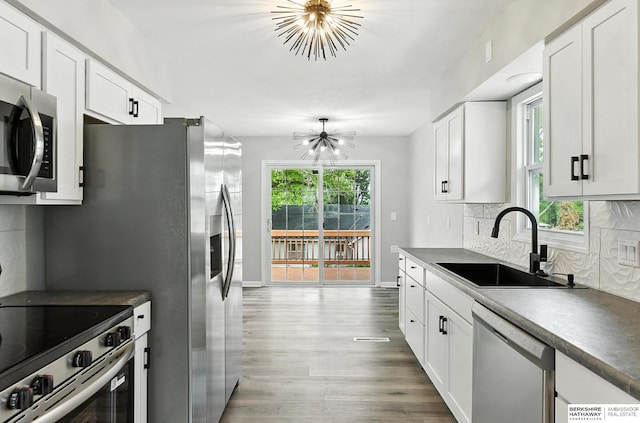 3080 S 48th St, Omaha, NE 68106 - kitchen with appliances with stainless steel finishes, a chandelier, wood finished floors, tasteful backsplash, and white cabinetry