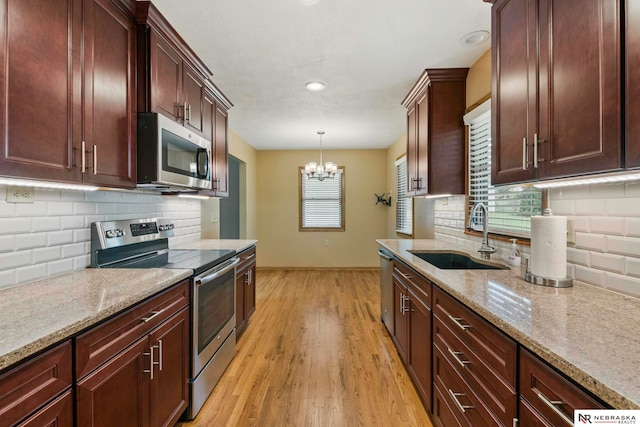 11018 Hascall St, Omaha, NE 68144 - kitchen with stainless steel appliances, a chandelier, light wood-style floors, light stone counters, and tasteful backsplash