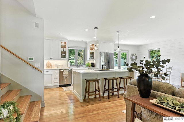 9903 Pasadena Ave, Omaha, NE 68124 - kitchen with appliances with stainless steel finishes, light countertops, light wood finished floors, a breakfast bar area, and glass insert cabinets