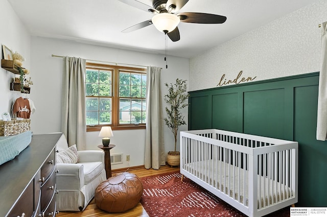9903 Pasadena Ave, Omaha, NE 68124 - bedroom with wood finished floors, a crib, a decorative wall, wainscoting, and ceiling fan