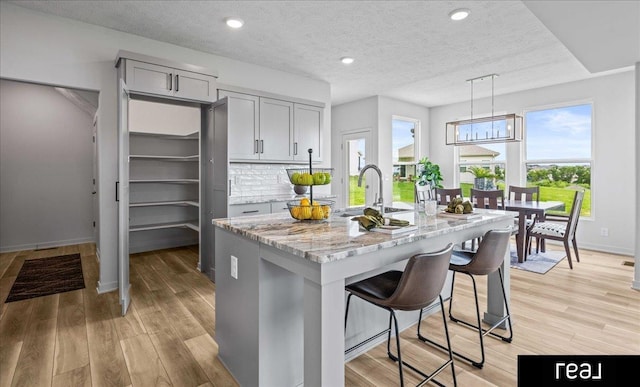 7409 N 176th Ave, Bennington, NE 68007 - kitchen with gray cabinets, light stone countertops, a center island with sink, light wood-type flooring, and pendant lighting