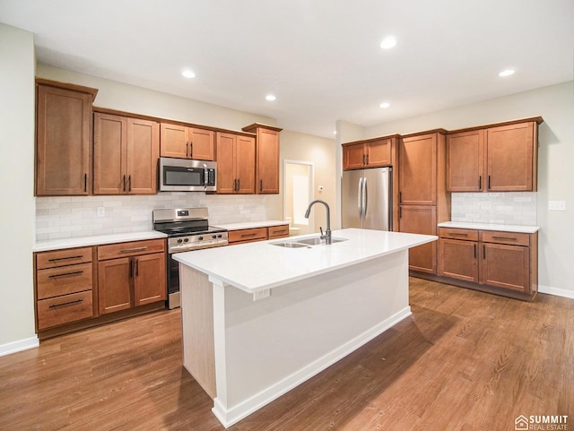 1120 Titan Dr, Hickman, NE 68372 - kitchen featuring stainless steel appliances, brown cabinetry, tasteful backsplash, a kitchen island with sink, and wood finished floors