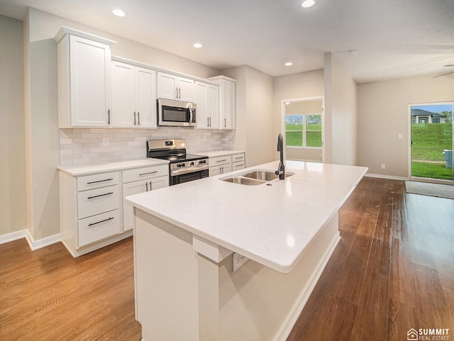 1130 Titan Dr, Hickman, NE 68372 - kitchen featuring appliances with stainless steel finishes, a center island with sink, wood finished floors, white cabinets, and decorative backsplash