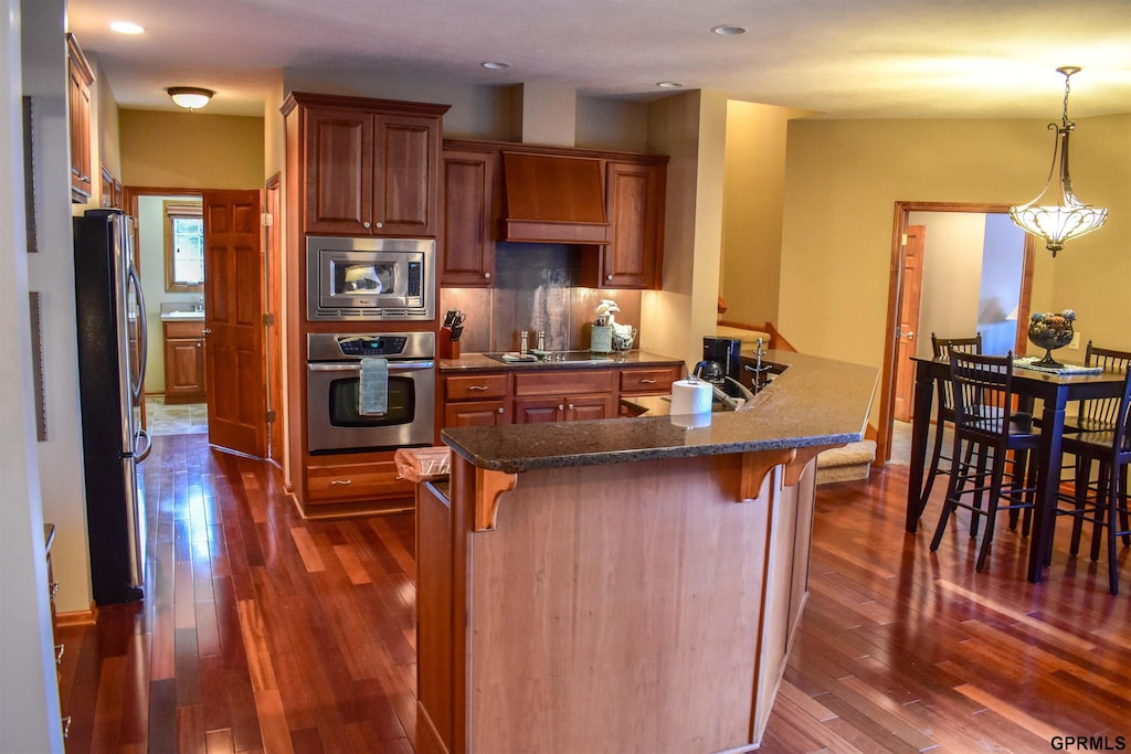 7841 Preserve Ln, Lincoln, NE 68516 - kitchen featuring appliances with stainless steel finishes, a kitchen bar, dark wood-type flooring, brown cabinets, and recessed lighting