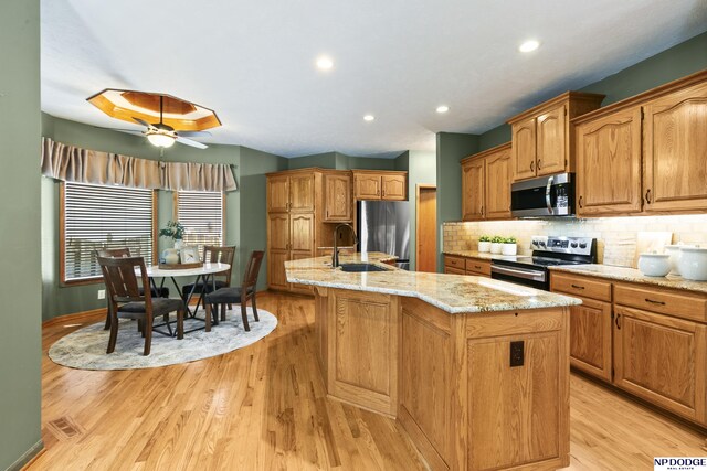 16367 Y St, Omaha, NE 68135 - kitchen featuring stainless steel appliances, light wood-type flooring, an island with sink, tasteful backsplash, and a ceiling fan