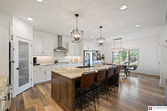 21034 X St, Omaha, NE 68022 - kitchen with wall chimney range hood, recessed lighting, a breakfast bar area, white cabinets, and wood finished floors