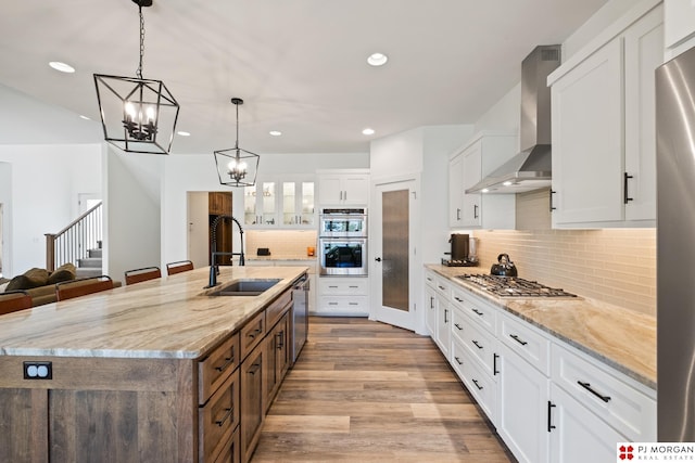 21034 X St, Omaha, NE 68022 - kitchen featuring appliances with stainless steel finishes, wall chimney range hood, a spacious island, a chandelier, and white cabinets