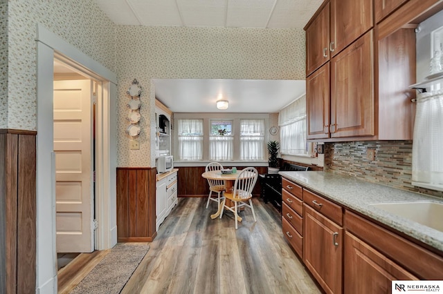 6409 Logan Ave, Lincoln, NE 68507 - kitchen with wainscoting, light wood-style flooring, wallpapered walls, brown cabinets, and white microwave