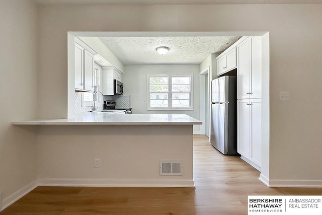 7025 S 41st St, Bellevue, NE 68147 - kitchen with stainless steel appliances, light wood-style flooring, light countertops, a peninsula, and white cabinetry