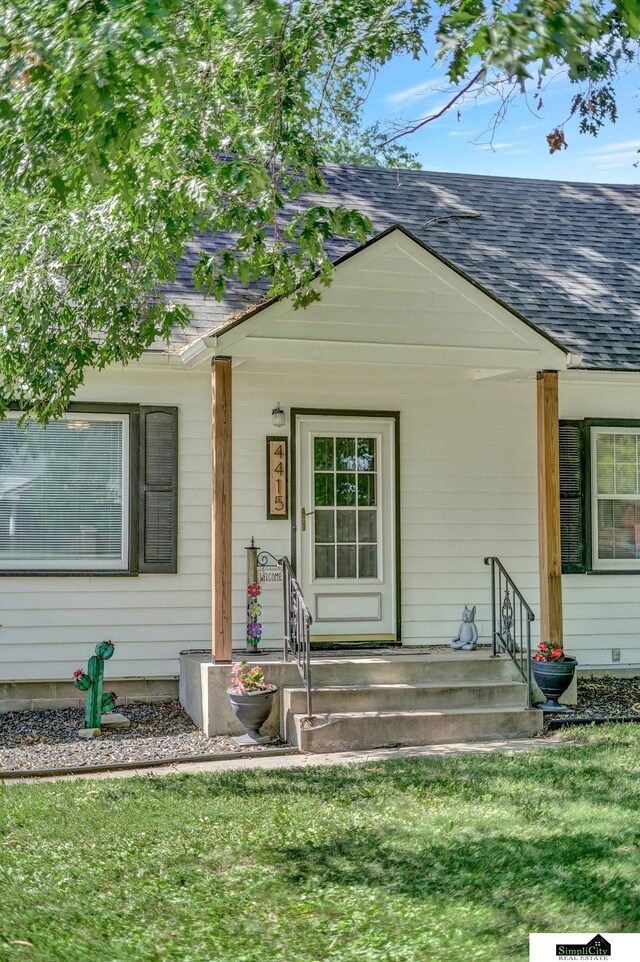 4415 S St, Lincoln, NE 68506 - view of exterior entry with a shingled roof, a yard, and a porch