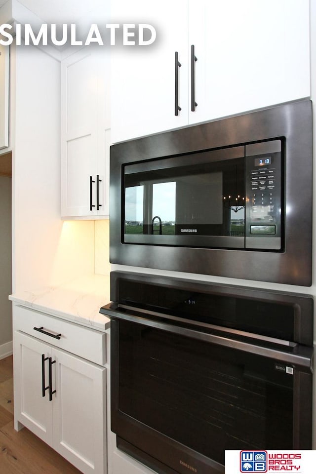 941 N 104th St, Lincoln, NE 68527 - kitchen view of stainless steel microwave, oven, white cabinetry, and light stone counters