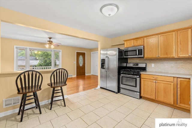 3052 S 46th Ave, Omaha, NE 68106 - kitchen with appliances with stainless steel finishes, light countertops, decorative backsplash, ceiling fan, and a breakfast bar
