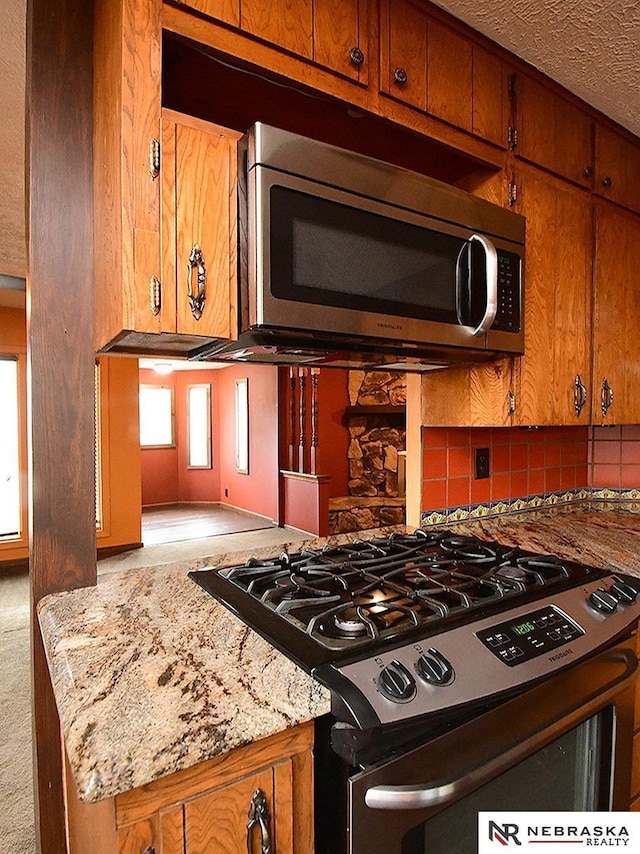 7626 S 41st St, Bellevue, NE 68147 - kitchen featuring appliances with stainless steel finishes, brown cabinets, decorative backsplash, light stone countertops, and a textured ceiling