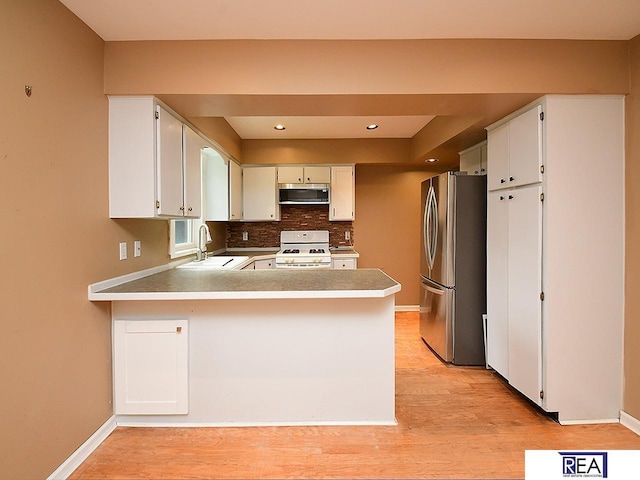 1312 N 148th Plz, Omaha, NE 68154 - kitchen featuring appliances with stainless steel finishes, a peninsula, light wood finished floors, decorative backsplash, and recessed lighting