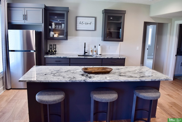 5445 Kestrel Pkwy, Omaha, NE 68022 - kitchen with freestanding refrigerator, a breakfast bar area, decorative backsplash, glass insert cabinets, and light wood-style floors