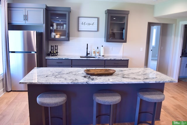5445 Kestrel Pkwy, Omaha, NE 68022 - kitchen with freestanding refrigerator, a breakfast bar, light wood finished floors, backsplash, and light stone countertops